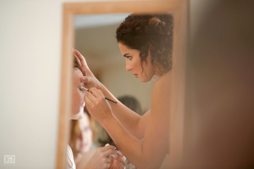 Hair and Makeup Artist does eye makeup in a mirror