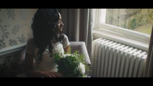 A bride looks out the window as she sits in her chair holding her bouquet