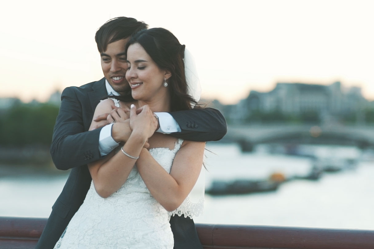 A couple embrace at sunset on a London bridge with the river Thames in the background