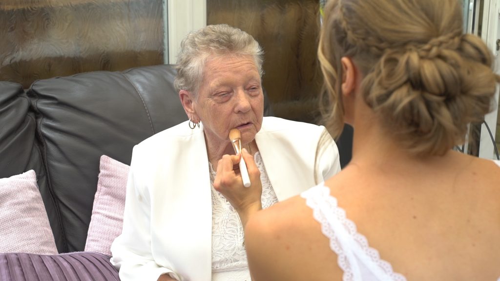 Grandmother has her makeup applied by a bridesmaid