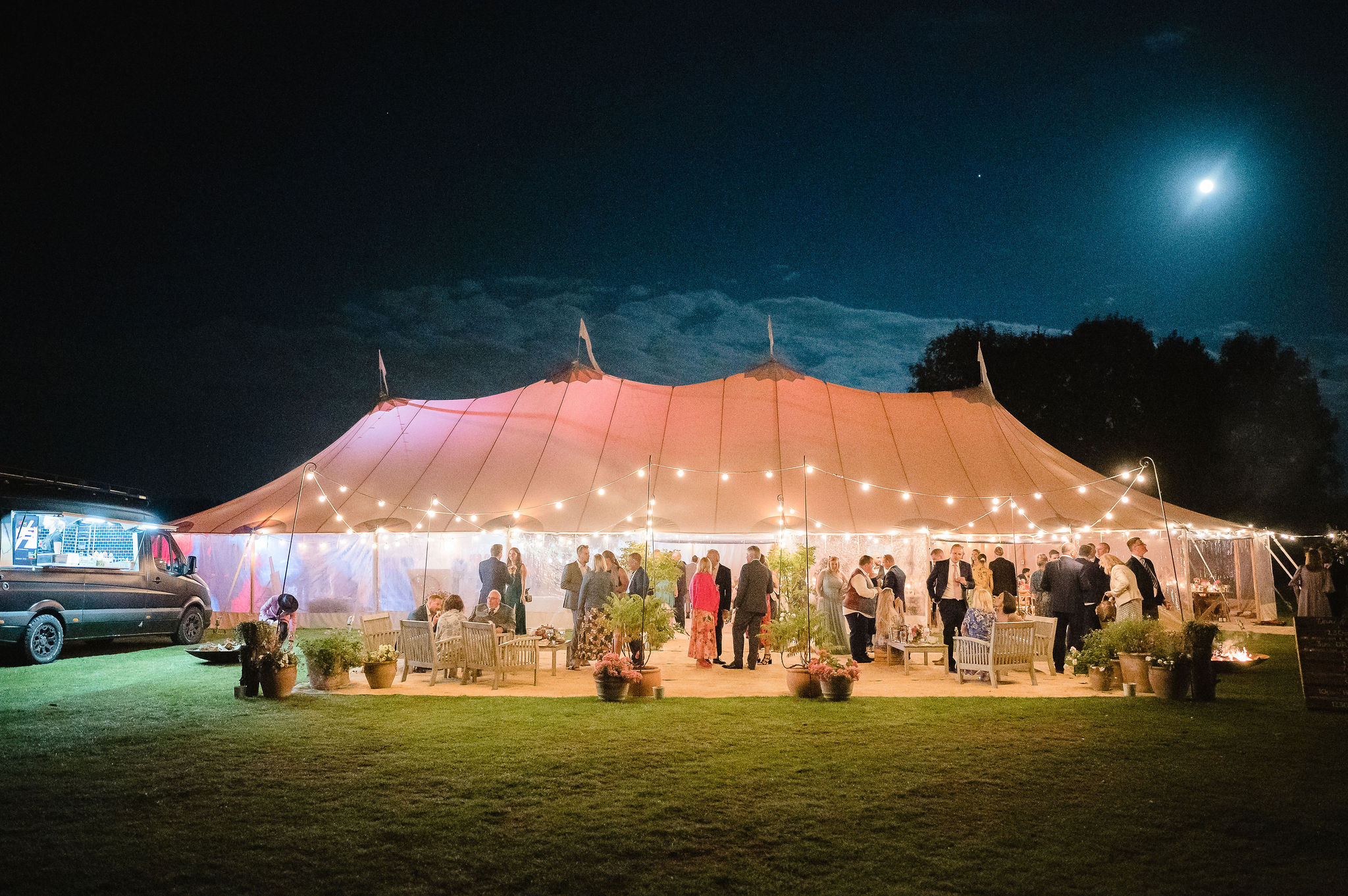 An outdoor marquee in a wedding is lit up in the evening sky