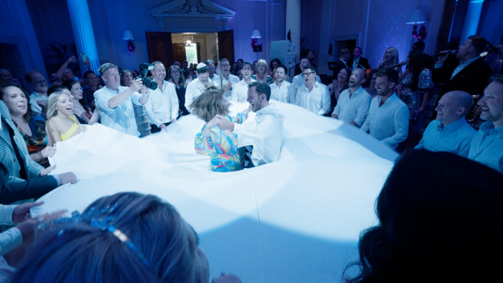 A mum and son dance inside a large Jewish wedding dresss on a blue lit dancefloor